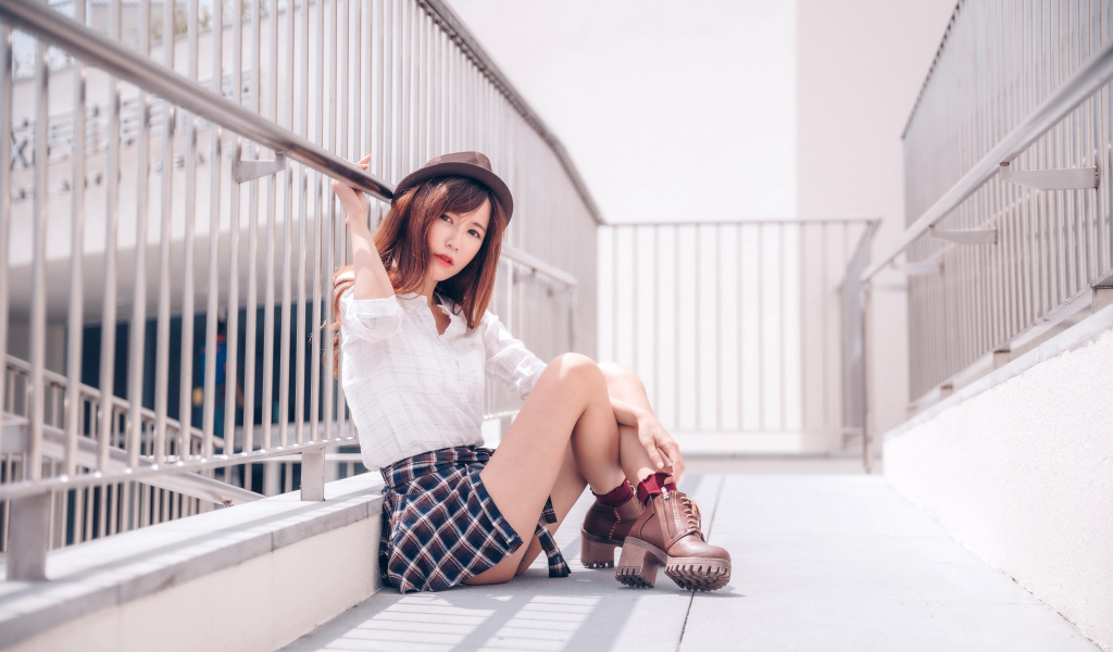Молодая азиатка в короткой юбке сидит у перил 