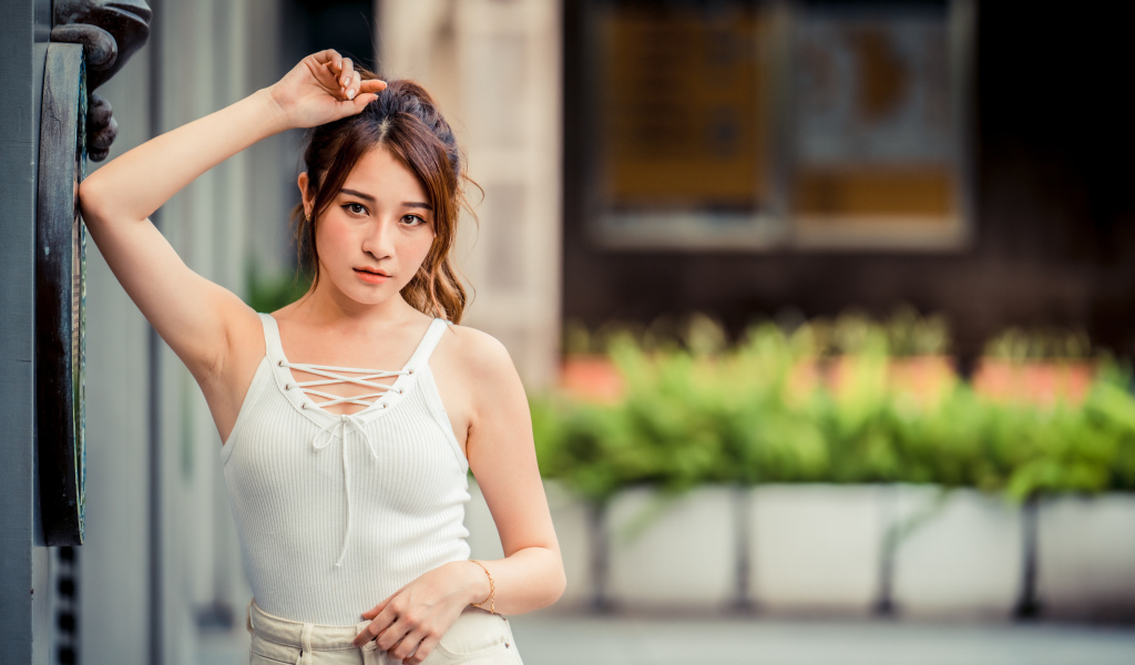 Молодая красивая азиатка в белой майке стоит у ворот