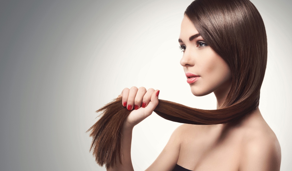 Молодая девушка держит в руках волосы на сером фоне