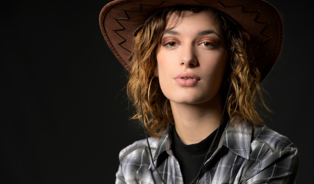 Молодая девушка в ковбойской шляпе на сером фоне