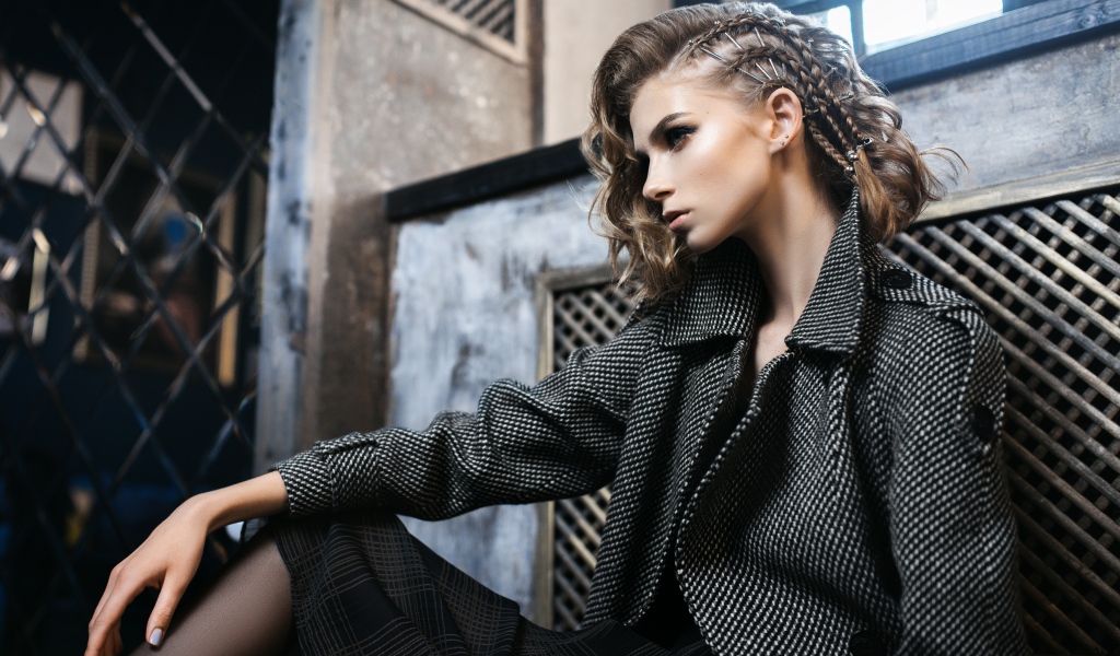 Молодая девушка в сером пальто сидит у стены