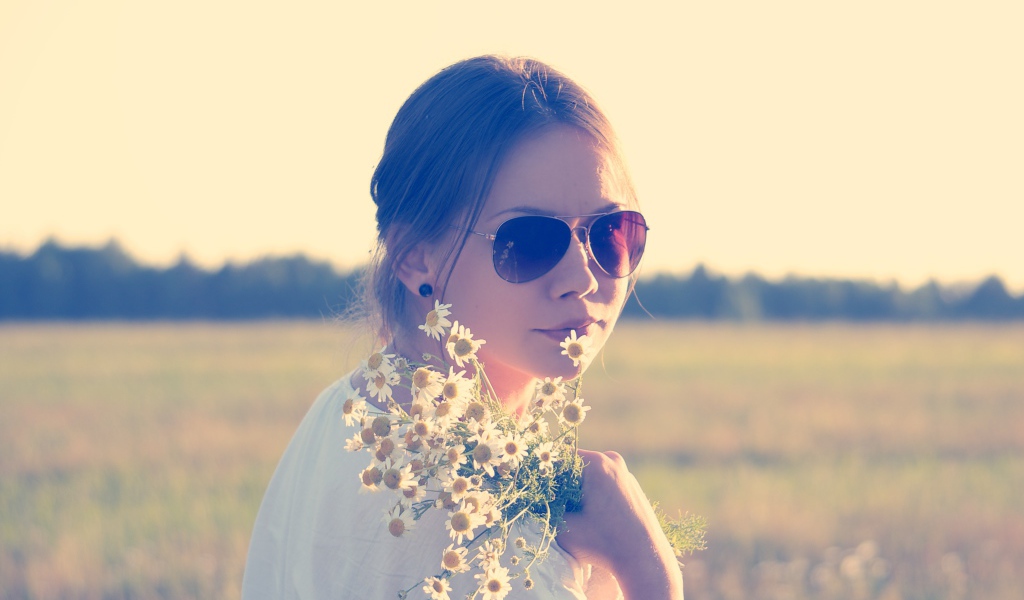 Молодая девушка в солнечных очках с букетом ромашек на поле