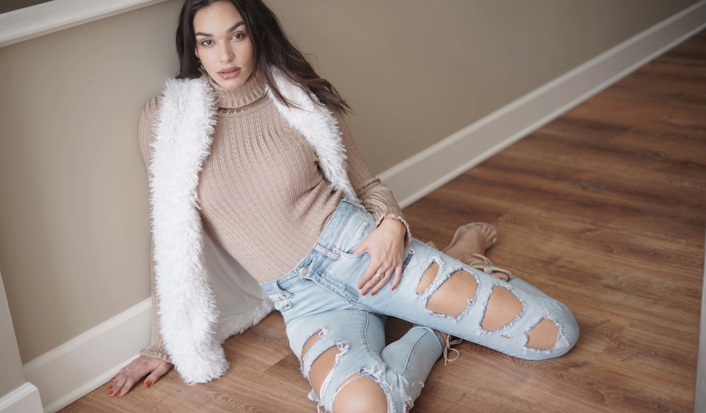 Молодая девушка в рваных джинсах сидит у стены