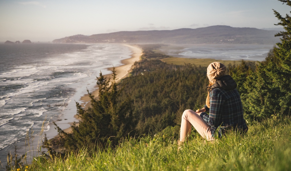 Молодая девушка сидит на зеленой траве на фоне моря