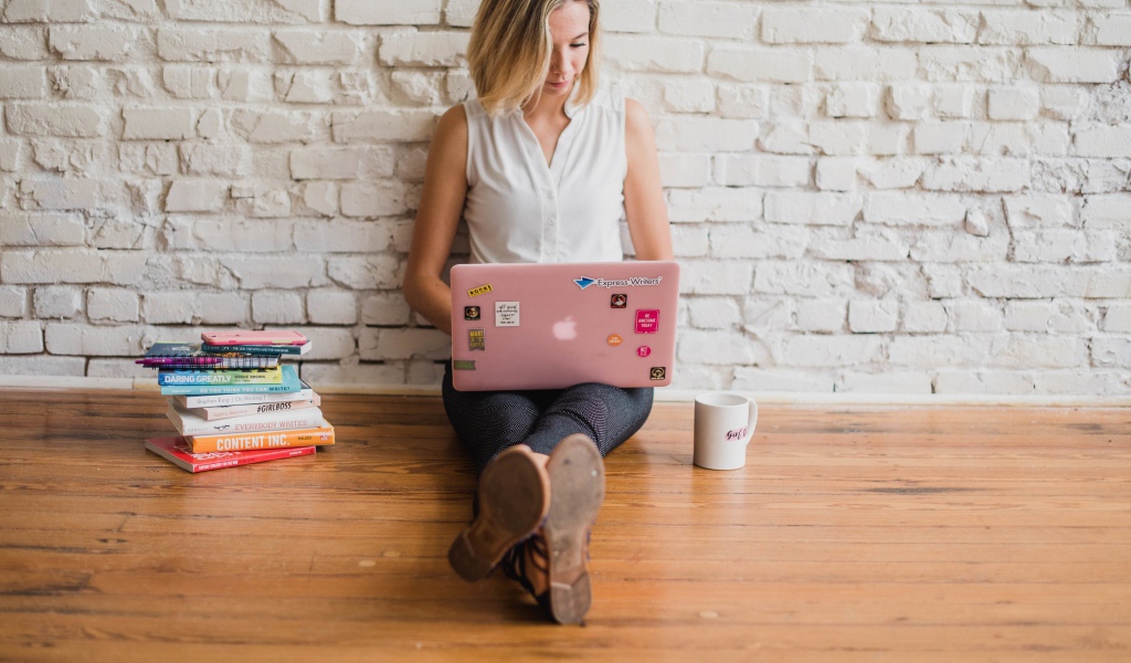 Молодая девушка студентка с ноутбуком и книгами у стены