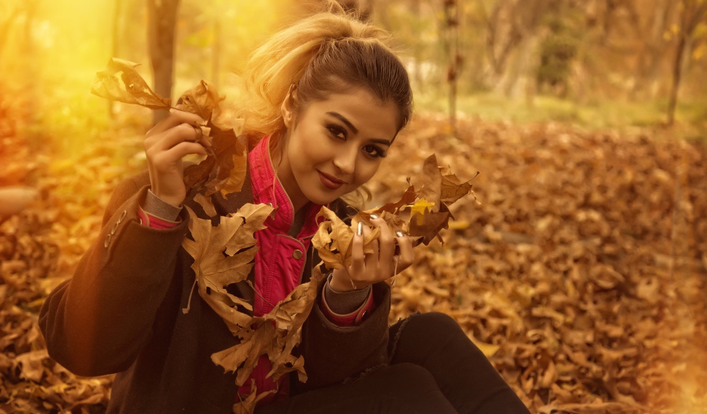 Молодая девушка с опавшими листьями в руках в парке
