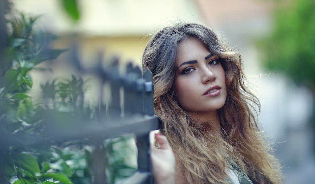 Молодая девушка с длинными волосами стоит у забора