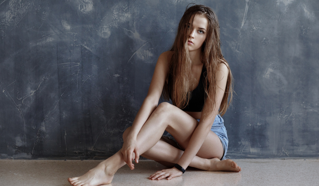 Молодая девушка с мокрыми волосами сидит у стены 