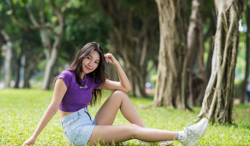 Молодая стройная азиатка сидит на земле в парке
