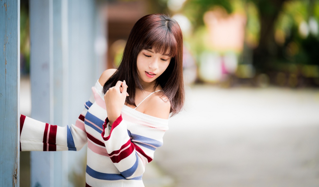 Молодая нежная девушка азиатка в свитере стоит у забора 