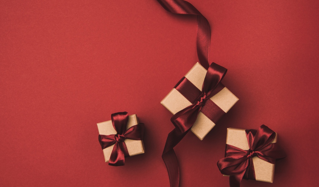 Три подарочные коробки с бантами на красном фоне