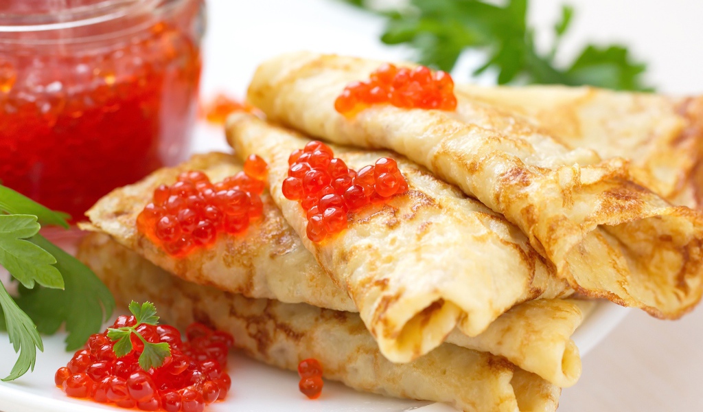 Аппетитные тонкие блины с красной икрой на тарелке с петрушкой угощение на Масленицу