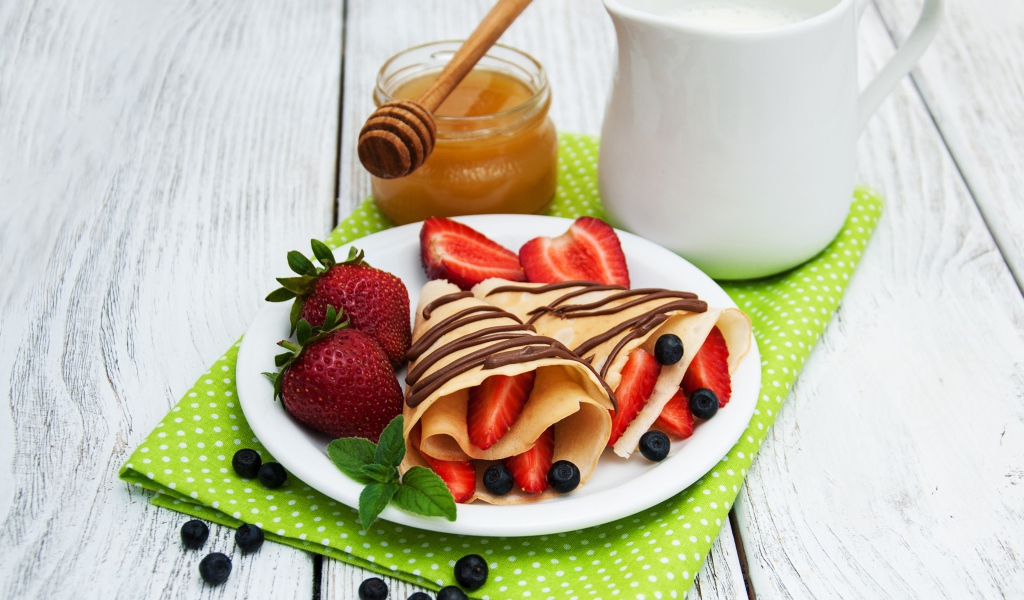 Вкусные блины с клубникой на столе с молоком и медом на праздник Масленица