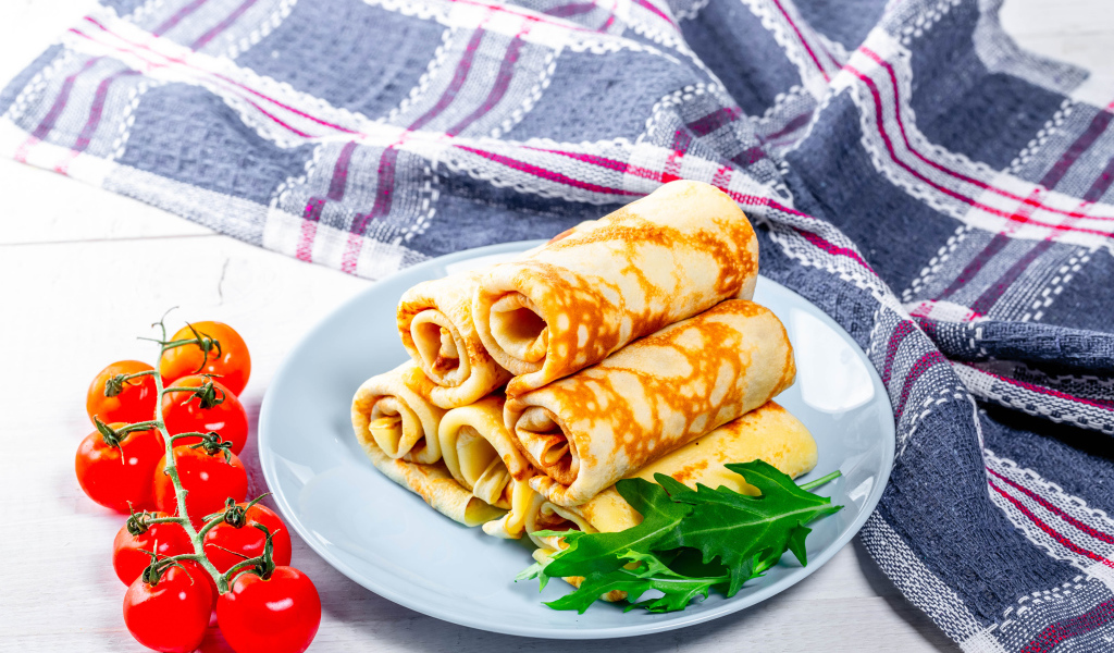 Блинчики на столе с помидорами и полотенцем угощение на Масленицу 2020