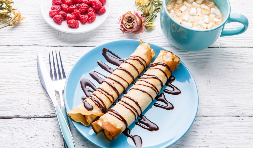 Тонкие блины с шоколадом на столе с ягодами малины и какао 