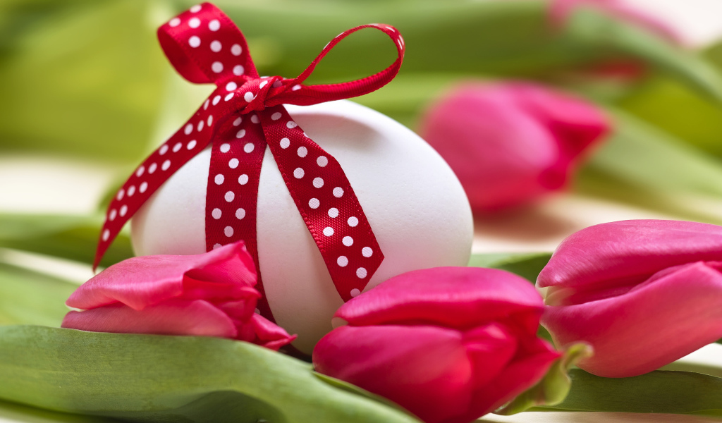 Яйцо с бантом на столе с тюльпанами на праздник Пасха