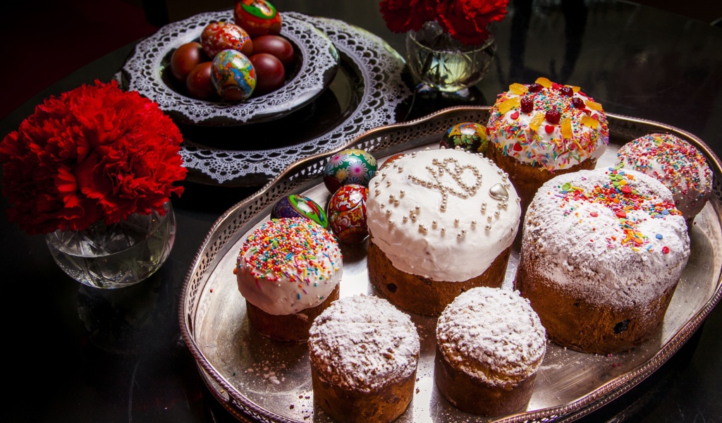 Много куличей на столе с гвоздиками и крашеными яйцами на праздник Пасха