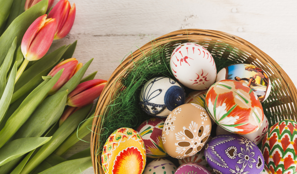 Разноцветные крашеные яйца в корзине с букетом тюльпанов на Пасху