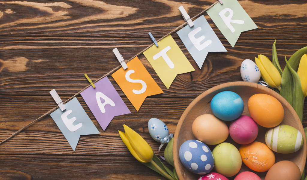 Надпись Пасха на столе с крашеными яйцами и тюльпанами