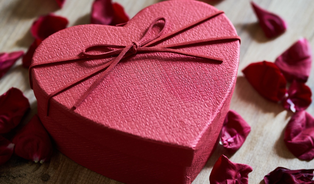 Большая красная коробка в форме сердца на столе с лепестками роз