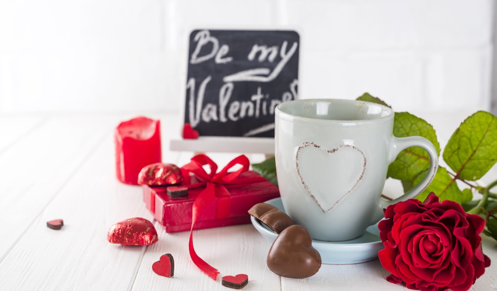 Белая чашка с конфетами и красной розой на столе в подарок на 14 февраля