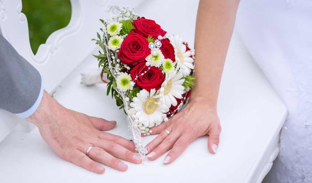 Две руки с обручальными кольцами и свадебным букетом