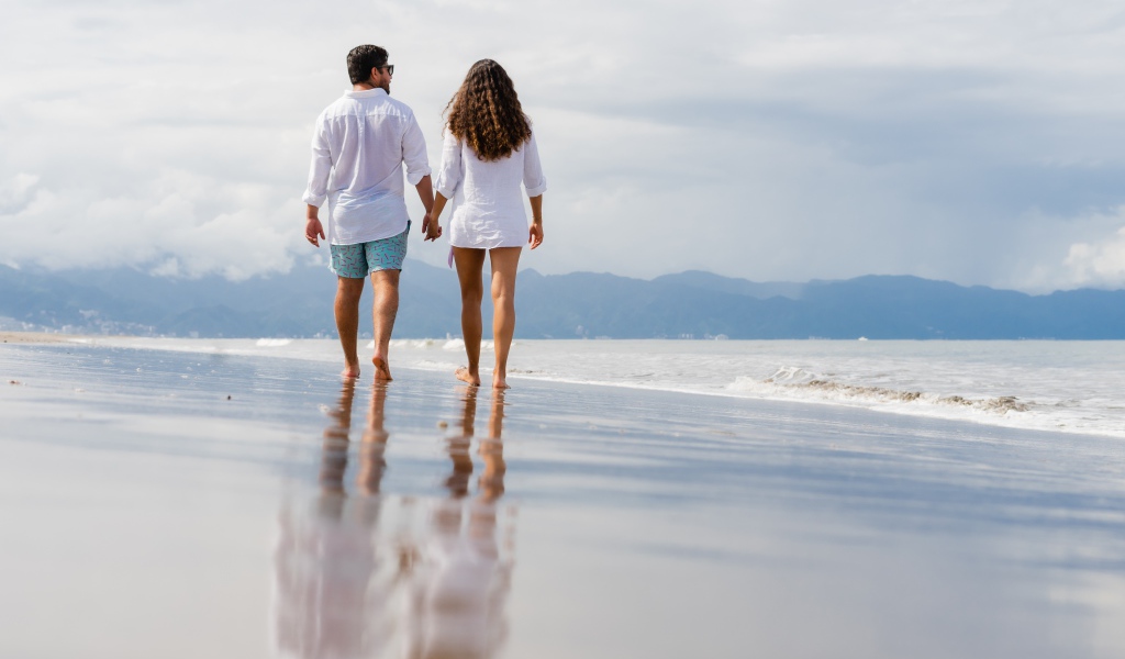 Влюбленная пара идет по мокрому песку у моря 