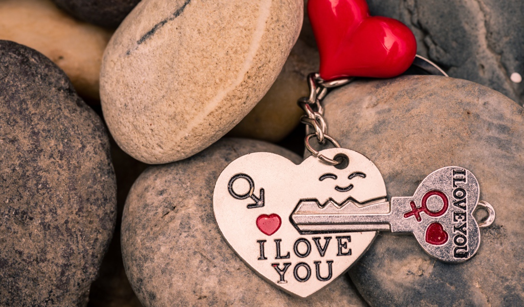 Брелок в форме сердца с ключом лежит на камнях 