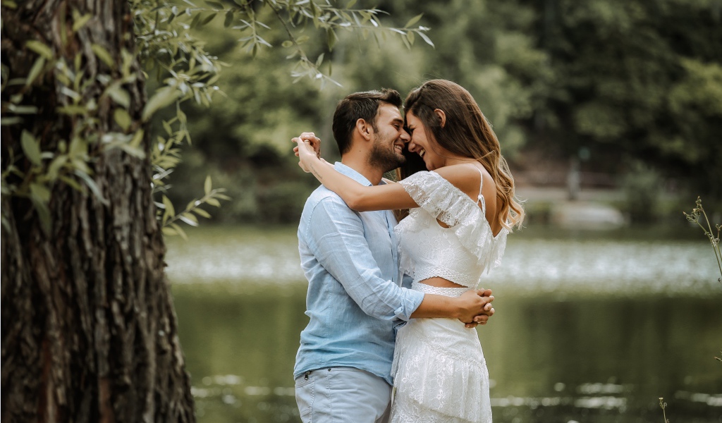 Влюбленная пара стоит у пруда в парке 