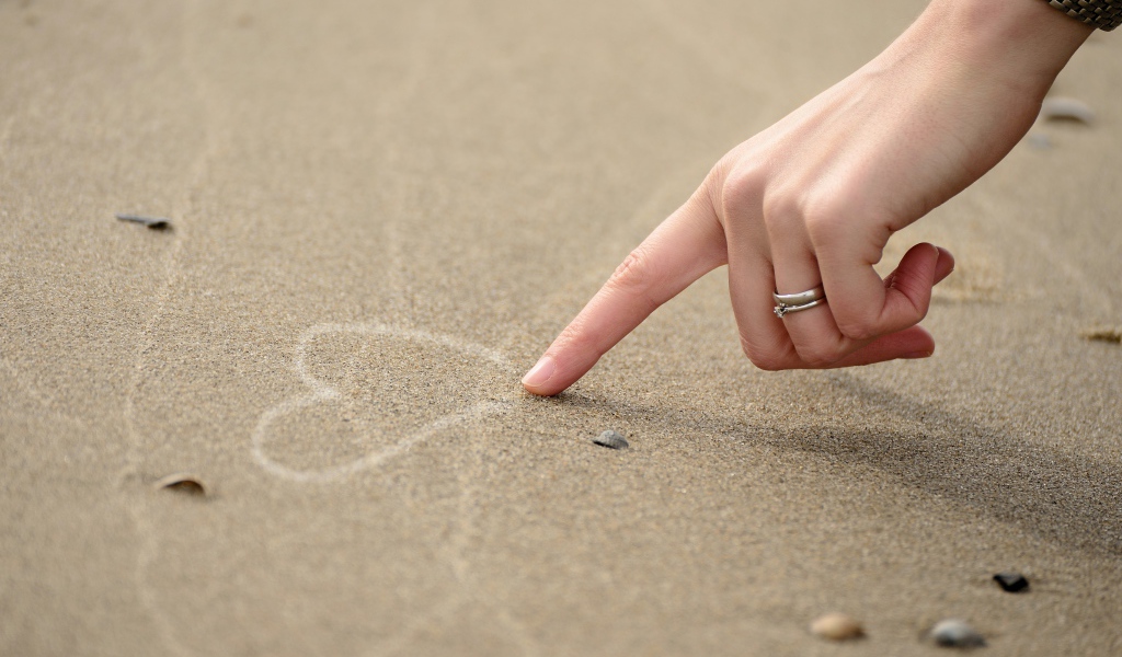 Девушка рисует сердце на песке 
