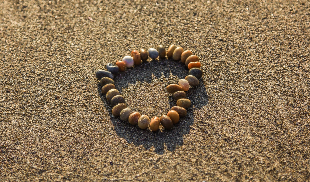 Сердце из мелкий морских камей на песке 