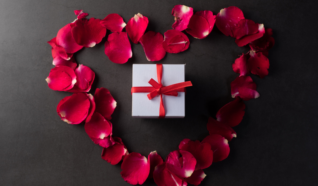 Сердце из красных лепестков розы с подарком на сером фоне