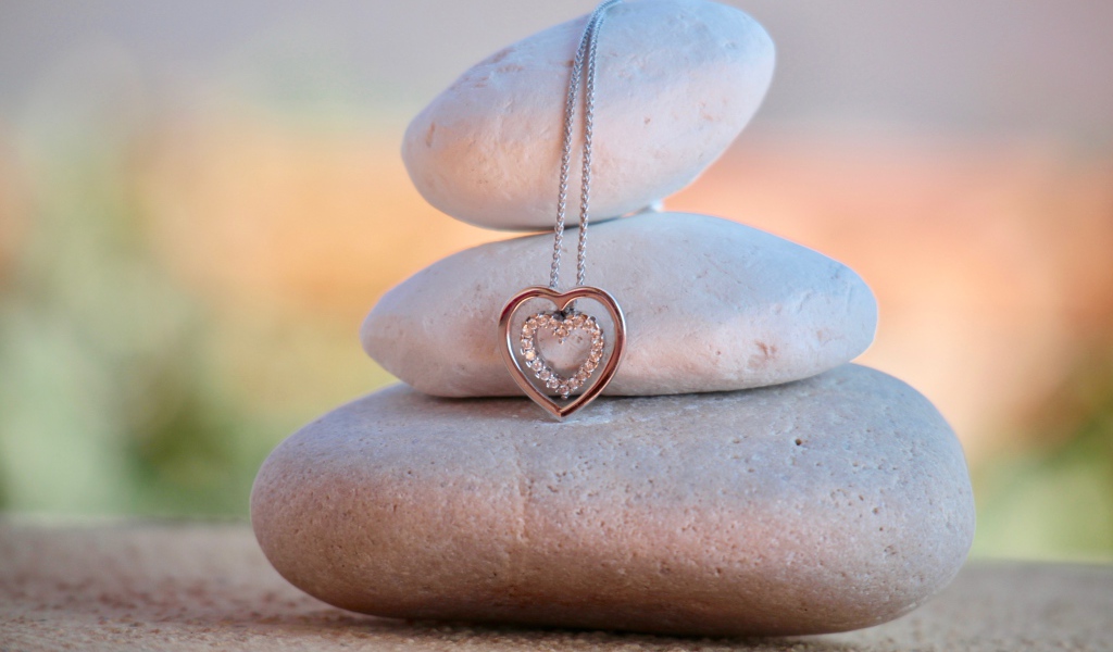 Золотой кулон в форме сердца висит на камнях 