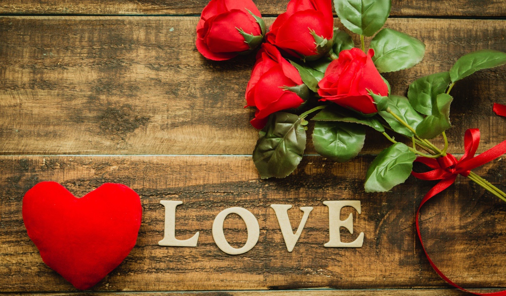 Надпись LOVE на столе с розами и красным сердцем
