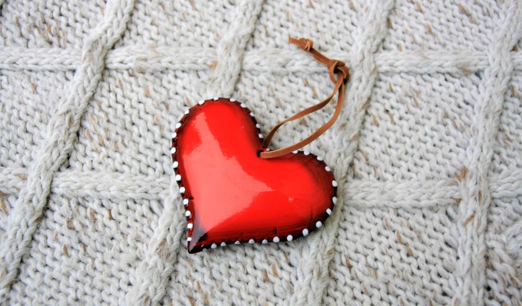 Красное сердце лежит на вязаном свитере 