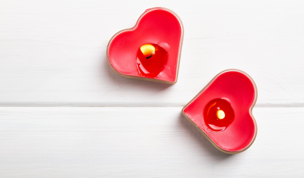 Two burning candles in the shape of a heart on the table