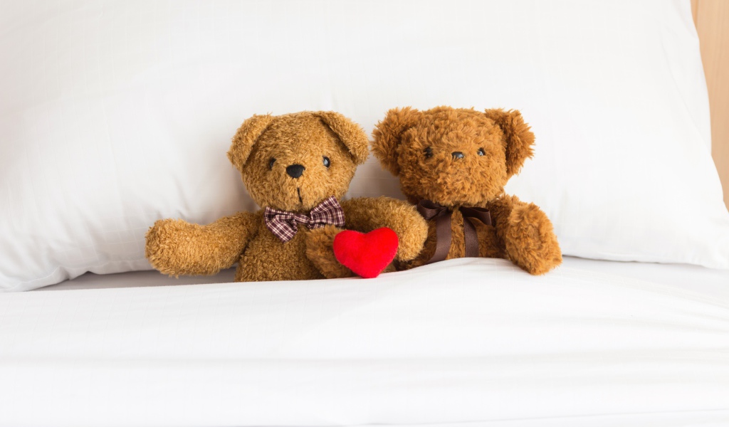 Два медвежонка Тедди лежат на кровати под одеялом 
