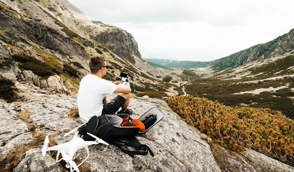 Парень с квадрокоптером сидит на камне в горах 