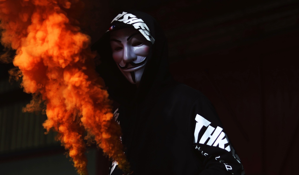 Мужчина в маске анонимуса с дымовой шашкой в руке