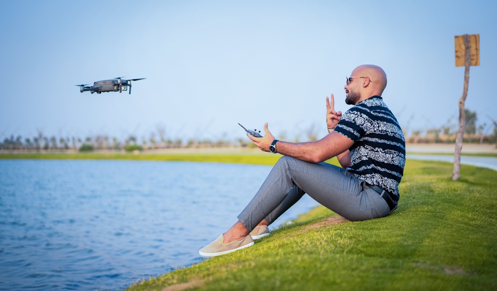 Мужчина запускает квадрокоптер над озером 
