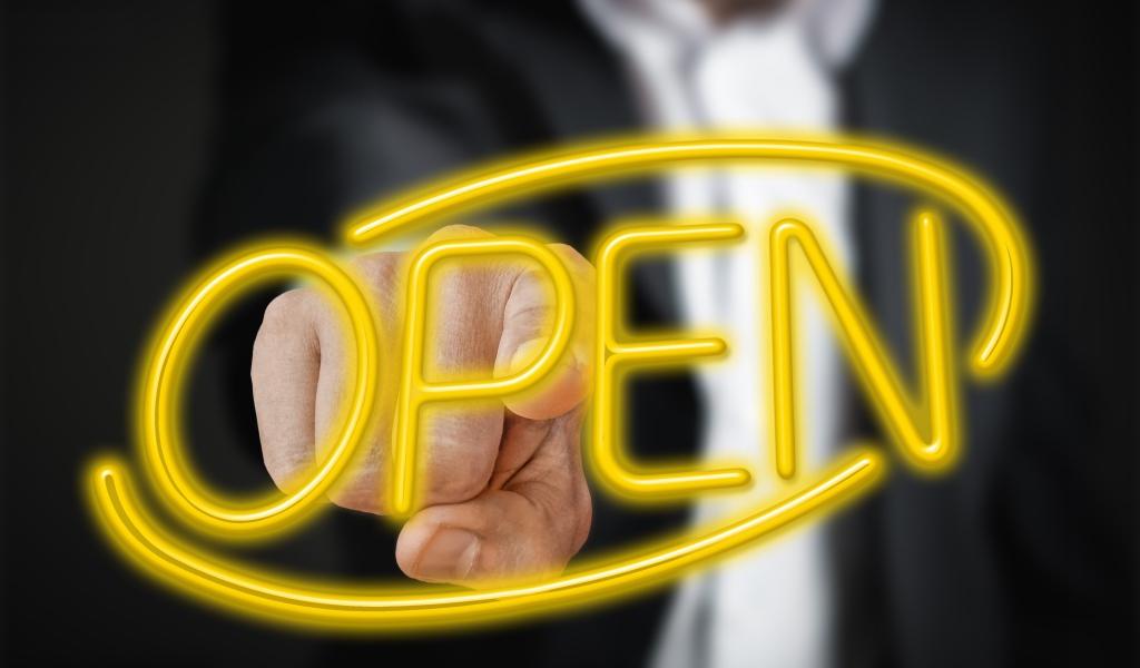 Мужчина трогает пальцем желтую  неоновую  надпись Open 