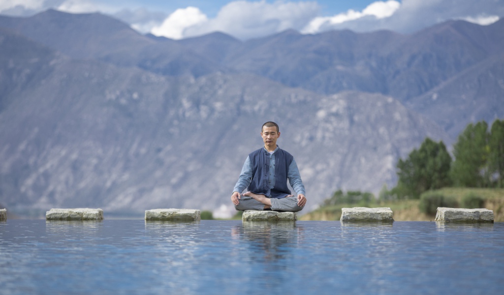 Мужчина азиат в позе лотоса медитирует у воды 