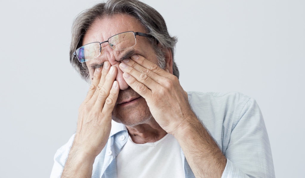 Пожилой мужчина трет глаза на сером фоне