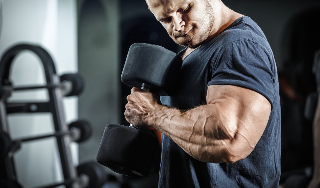 Мужчина бодибилдер в спортзале с гантелей 