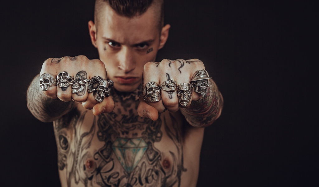 Мужчина с татуировками на теле с перстнями на пальцах