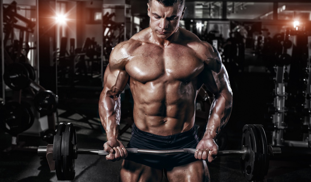 Мускулистый мужчина со штангой в руках в спортзале