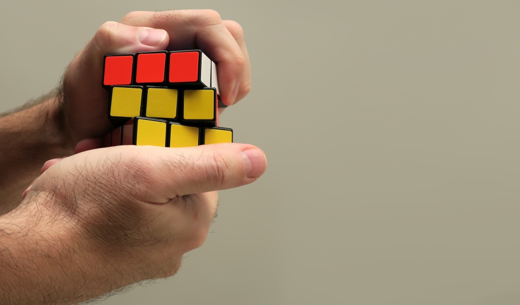 Кубик Рубика в руках мужчины на сером фоне