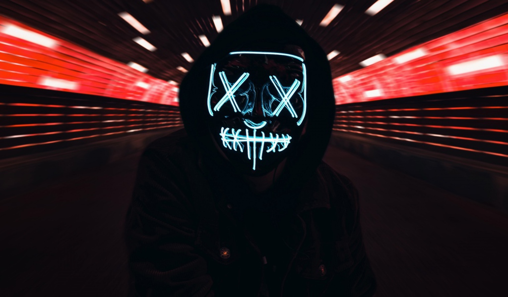 Парень в черной куртке в неоновой маске анонимуса на лице