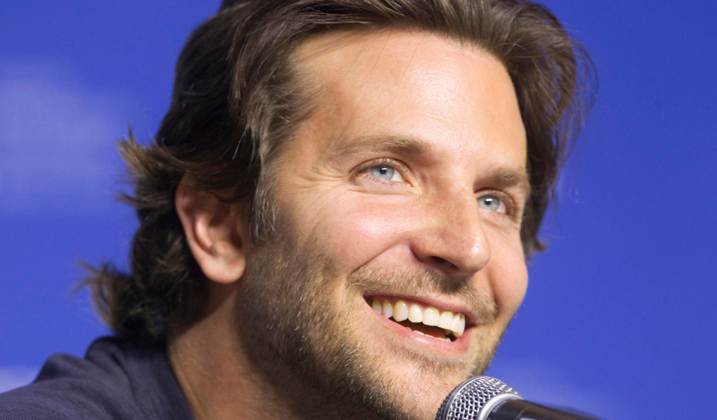 Голубоглазый актер Брэдли Купер с микрофоном на синем фоне