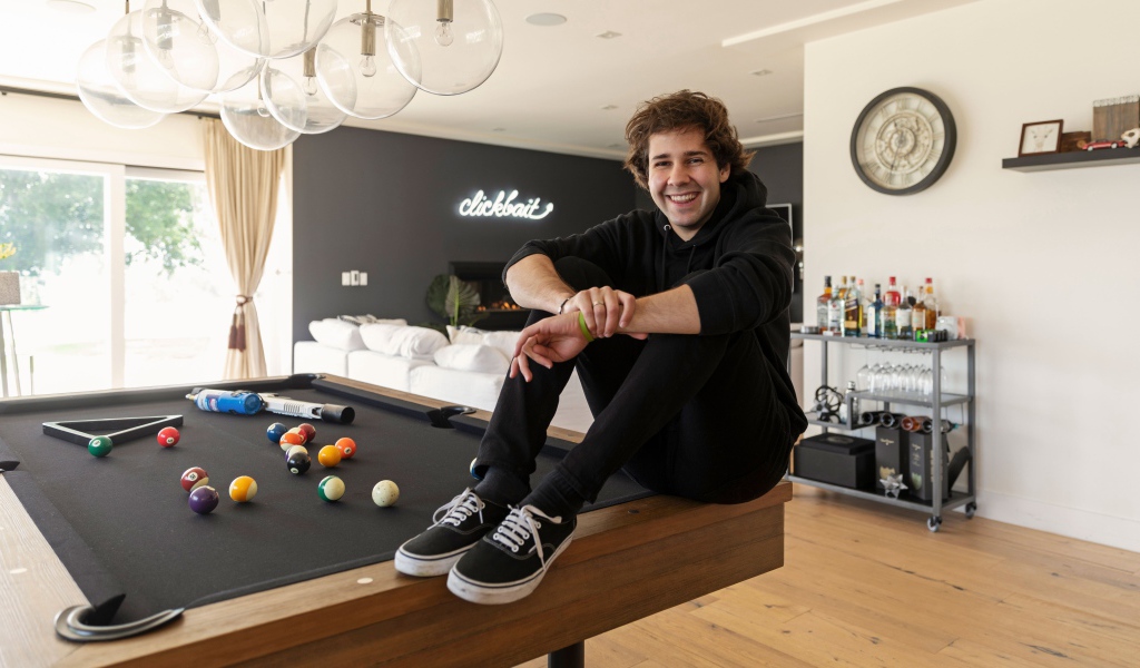 Молодой блогер, юморист  Дэвид Добрик сидит на столе